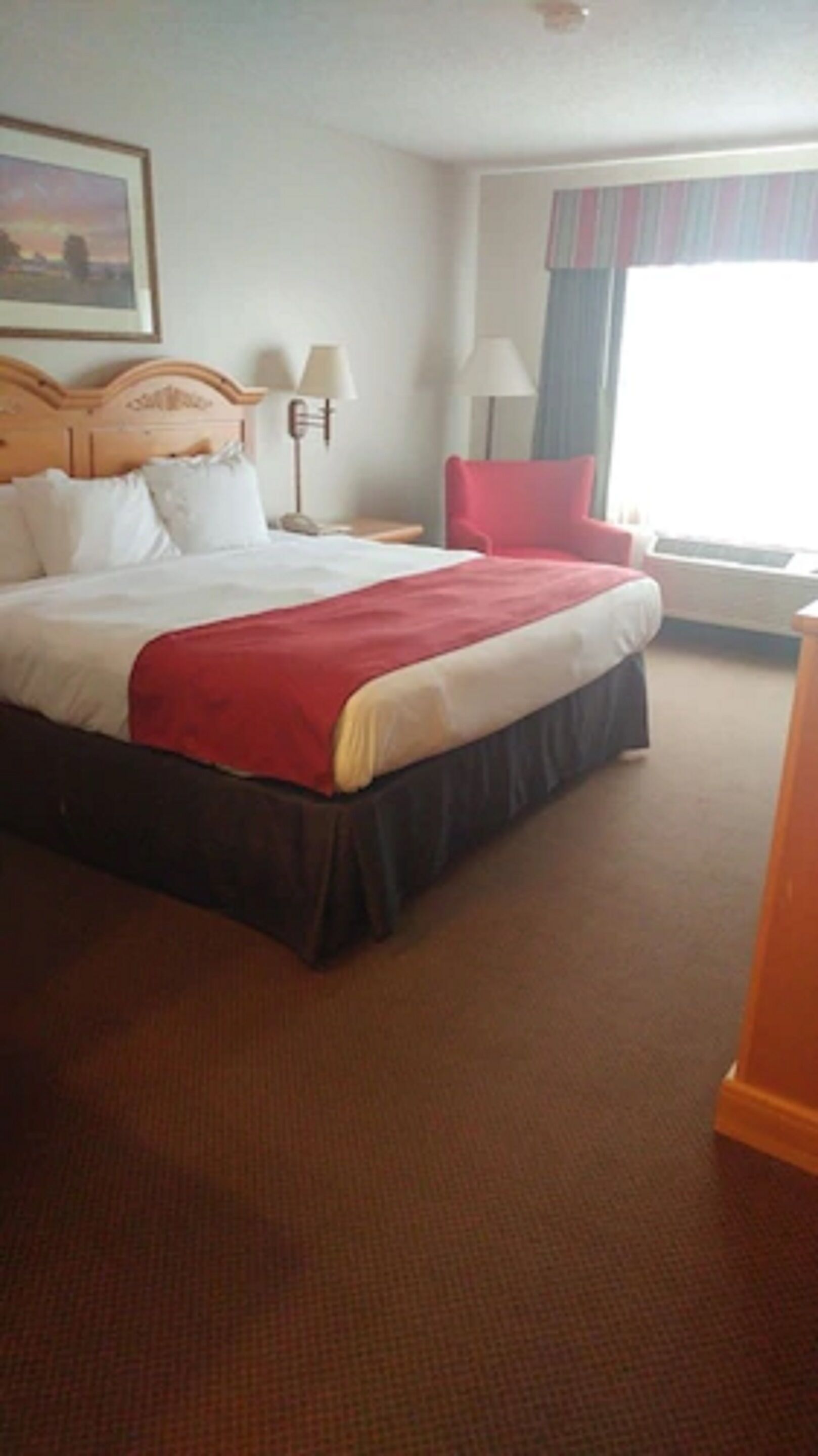 A hotel room with a large bed, a red chair, a desk, and a window with curtains.