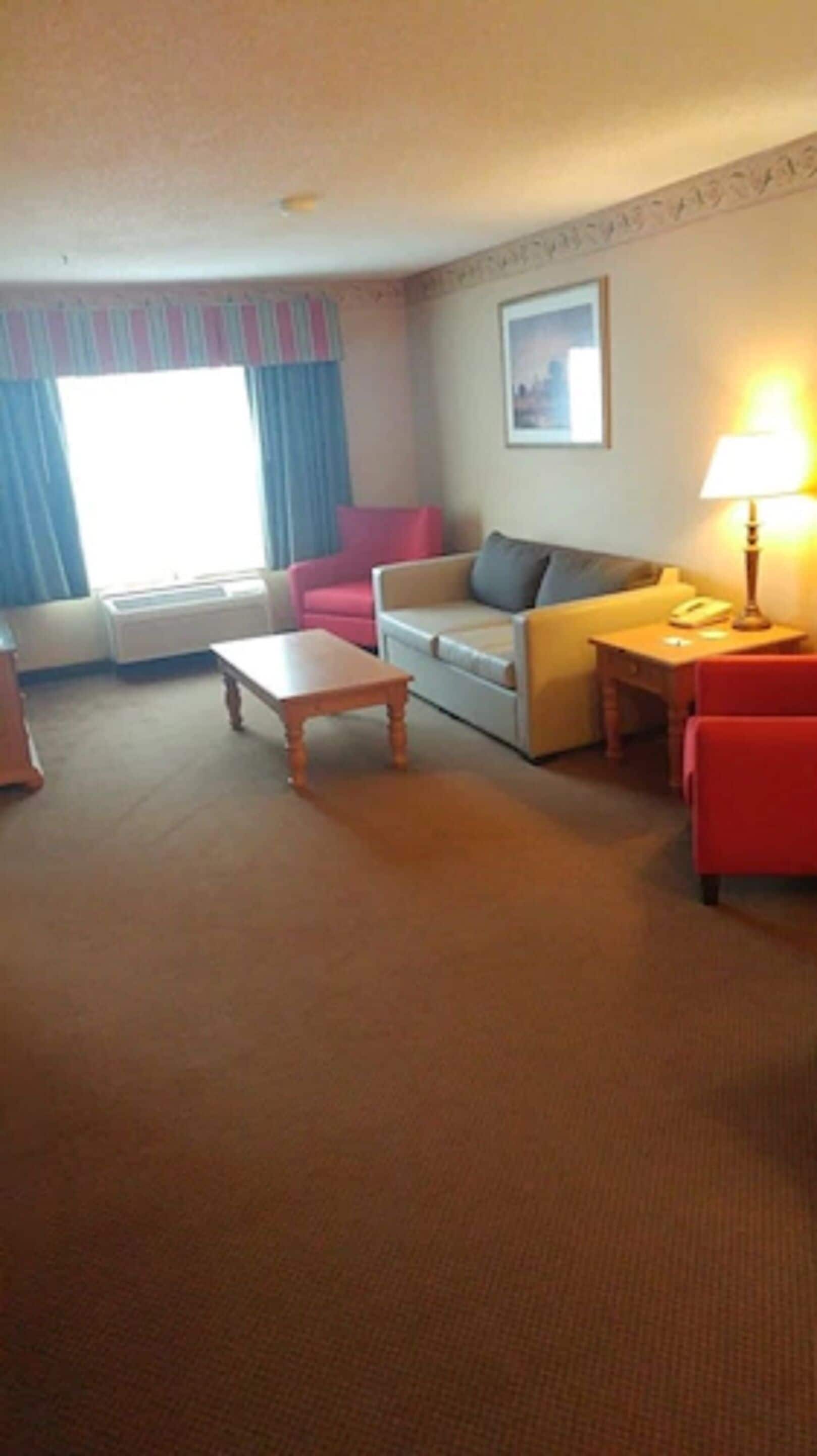 A living room with a sofa, a coffee table, a lamp, and a window with curtains.
