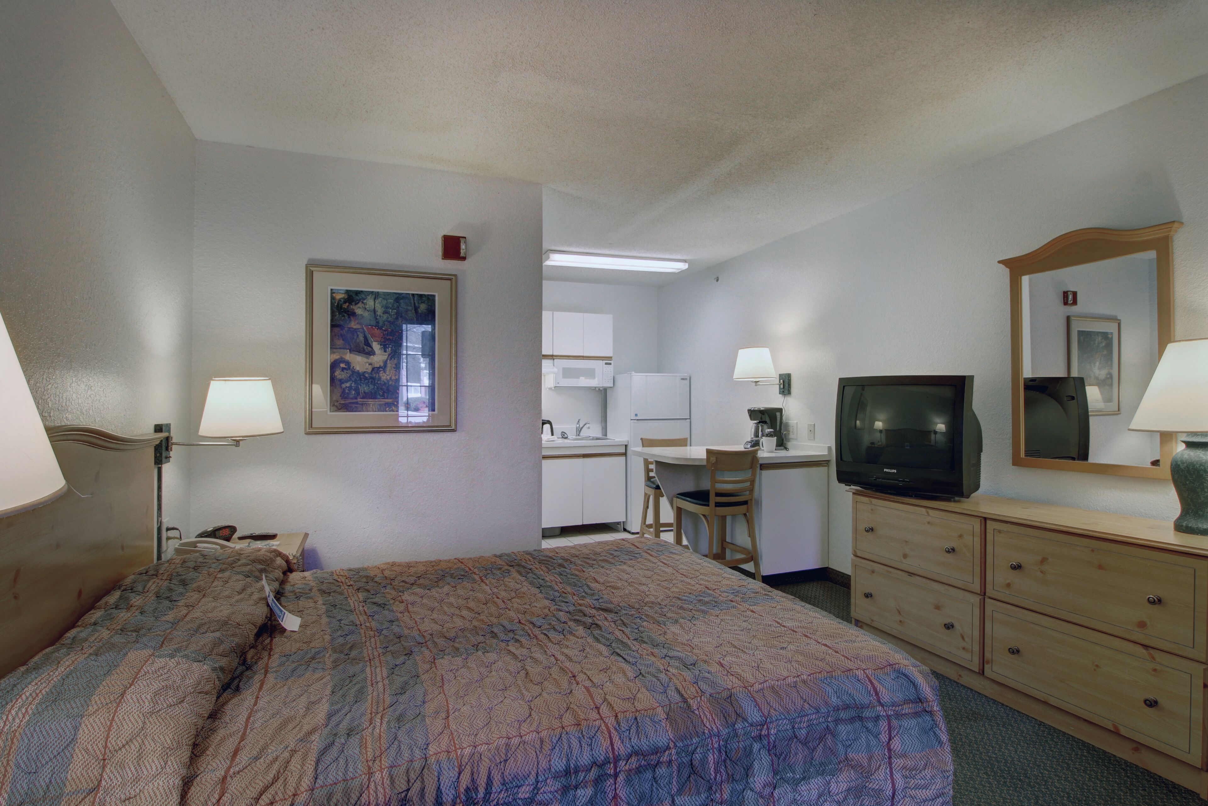 A hotel room with a bed, a desk, a television, and a dresser.