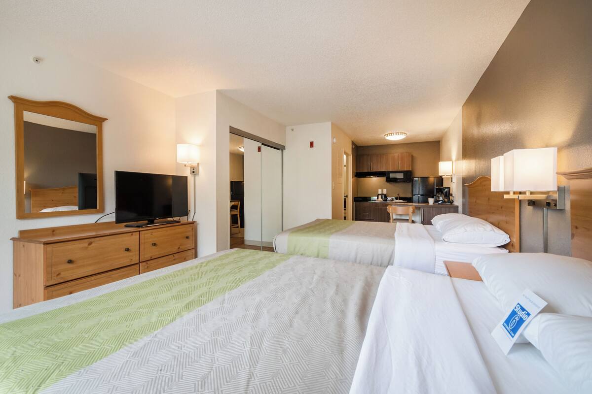 A hotel room with two beds, a TV, a dresser, and a kitchenette.