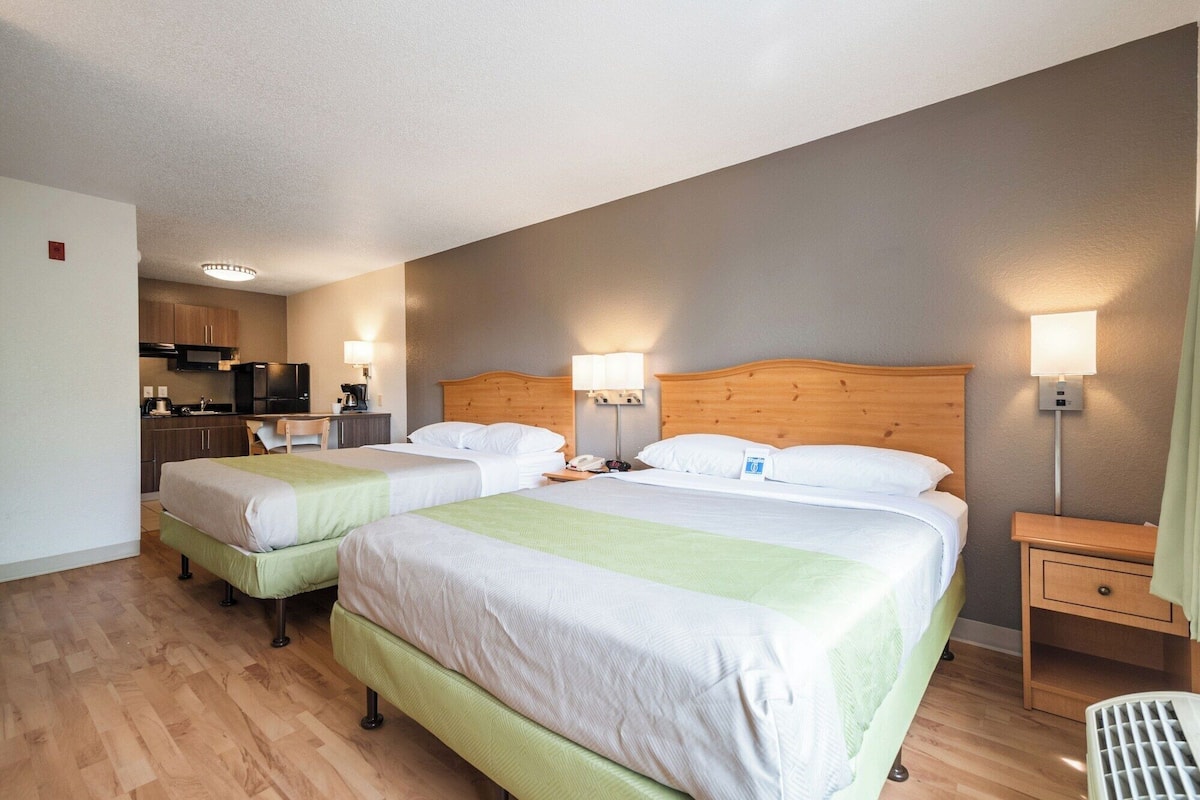 A hotel room with two beds, a kitchenette, and a bathroom.