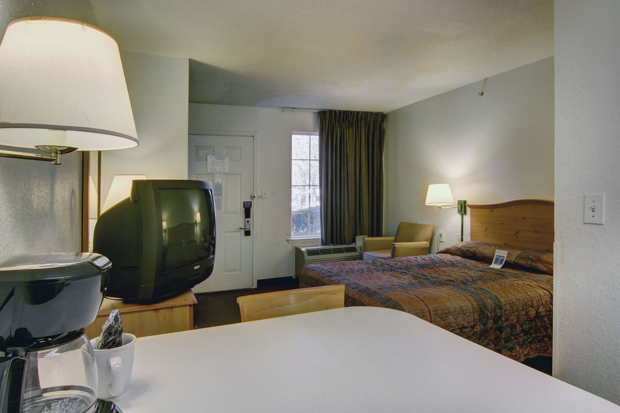 A hotel room with a bed, a television, a coffee maker, a chair, and a desk.