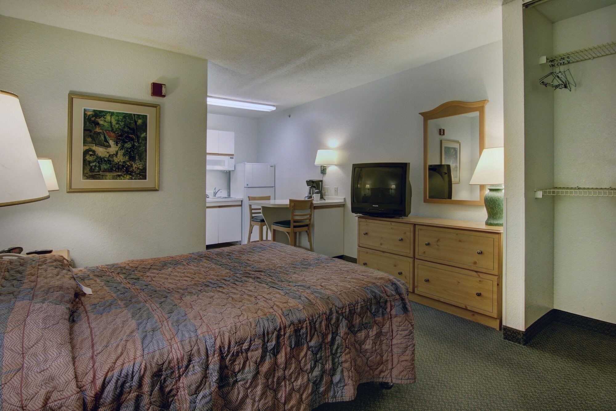 A hotel room with a bed, a desk, a television, and a dresser.