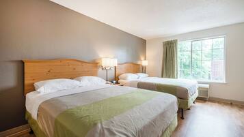 A hotel room with two beds, a wooden headboard, bedside lamps, a window with curtains, and a radiator.