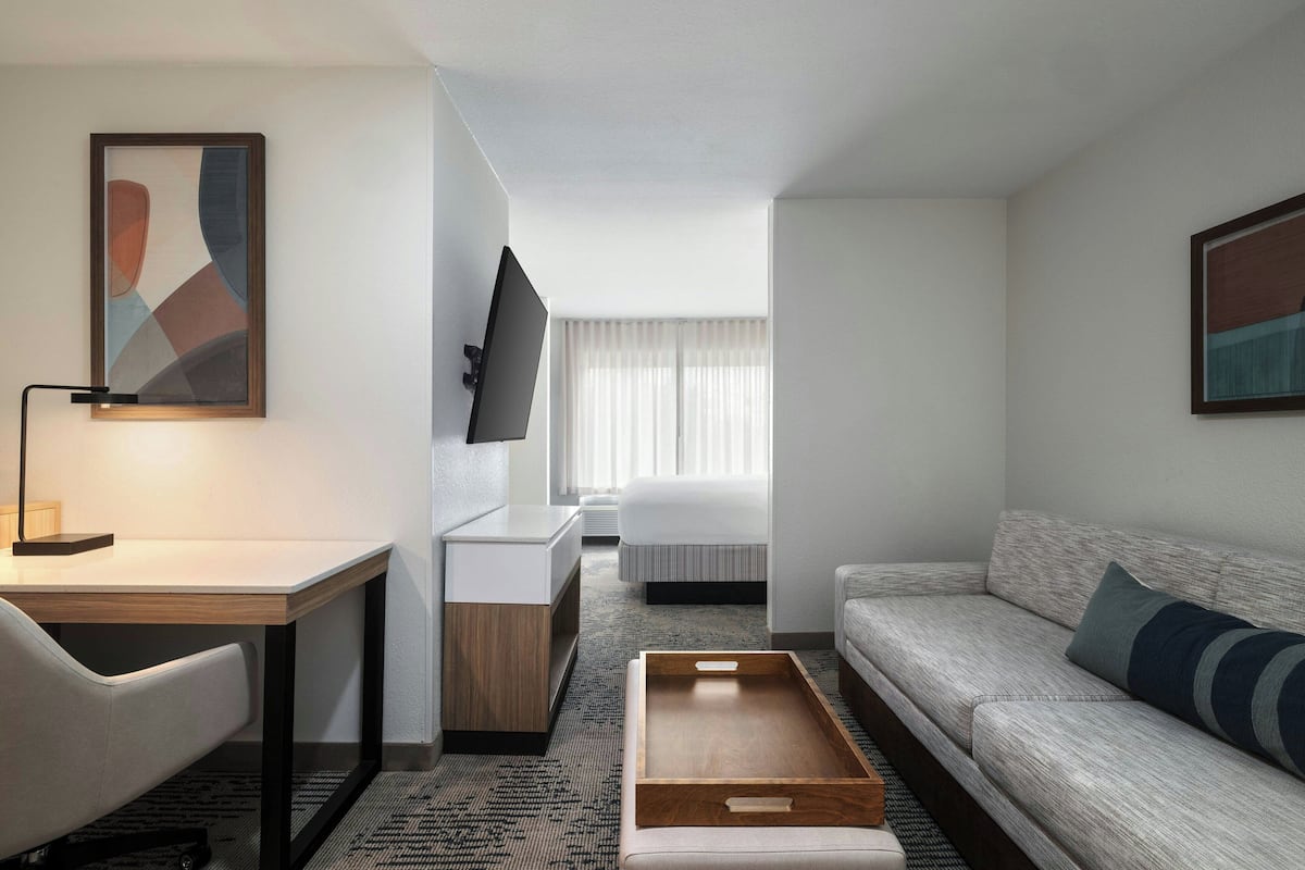 Ein Hotelzimmer mit Schreibtisch, einer Couch, einem Bett, einem Fernseher und Bildern an den Wänden.