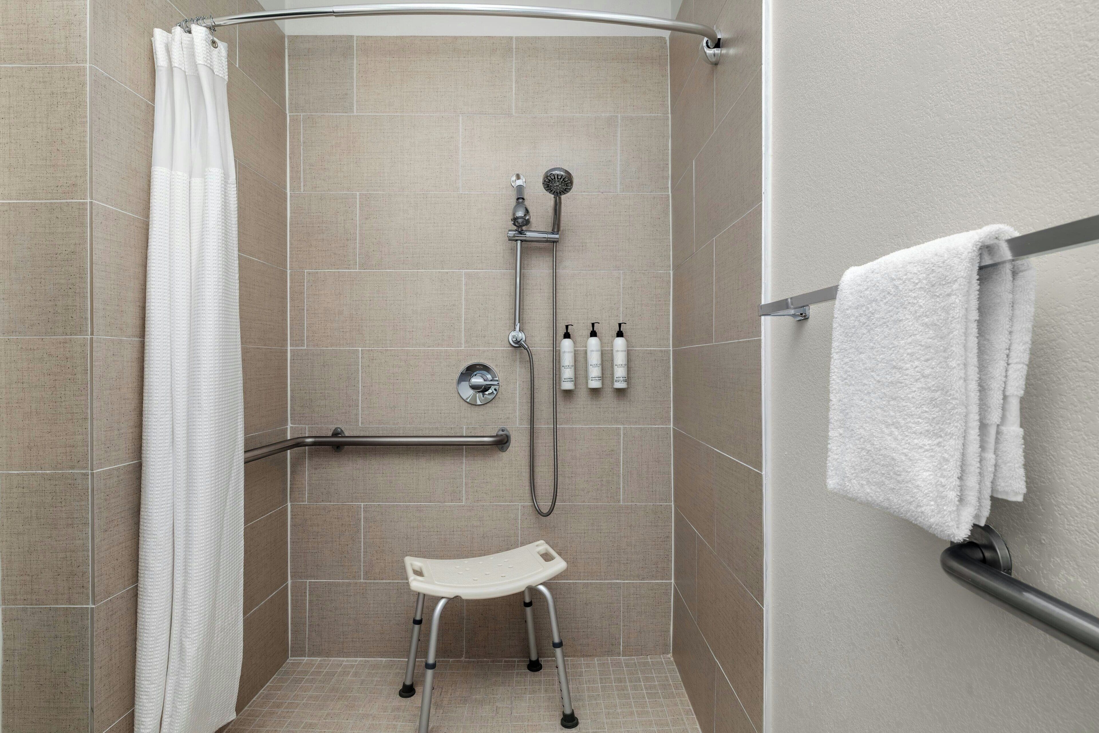 A shower area with a grab bar, a white towel rack, and a white shower seat.