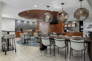 A modern dining area with a long table, multiple chairs, and hexagonal pendant lights. - SpringHill Suites Dallas Arlington North (Arlington)