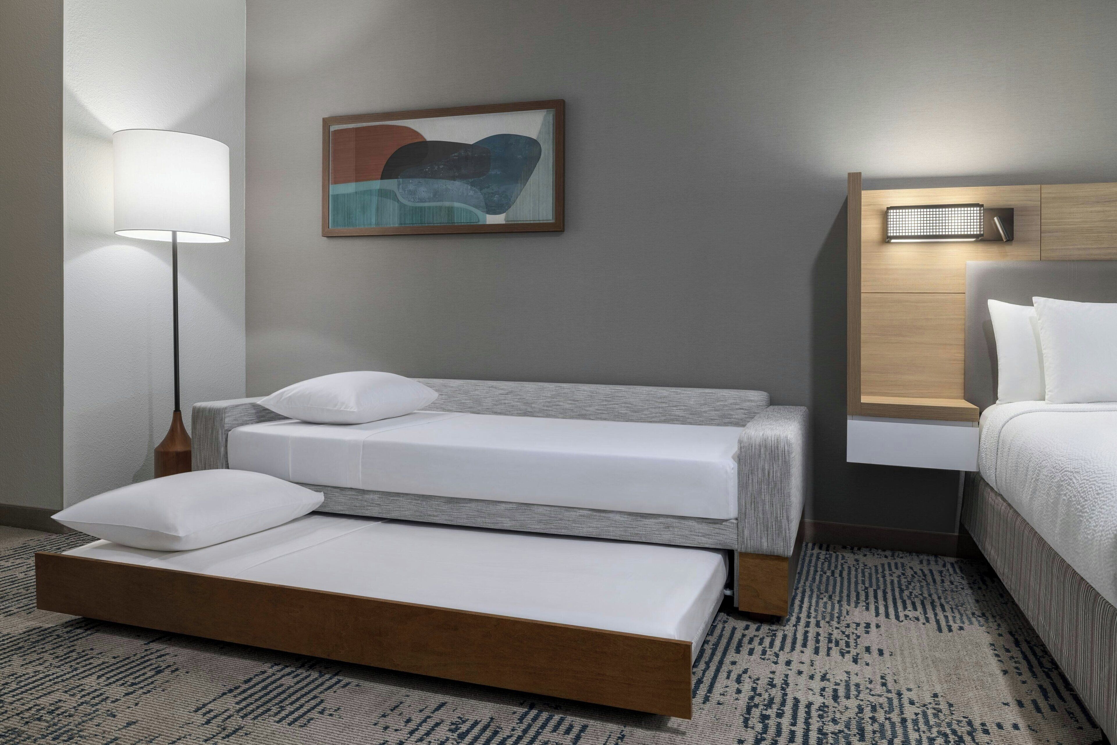 Een hotelkamer met een bed, nachtkastje, lamp, wandlamp en een schilderij.