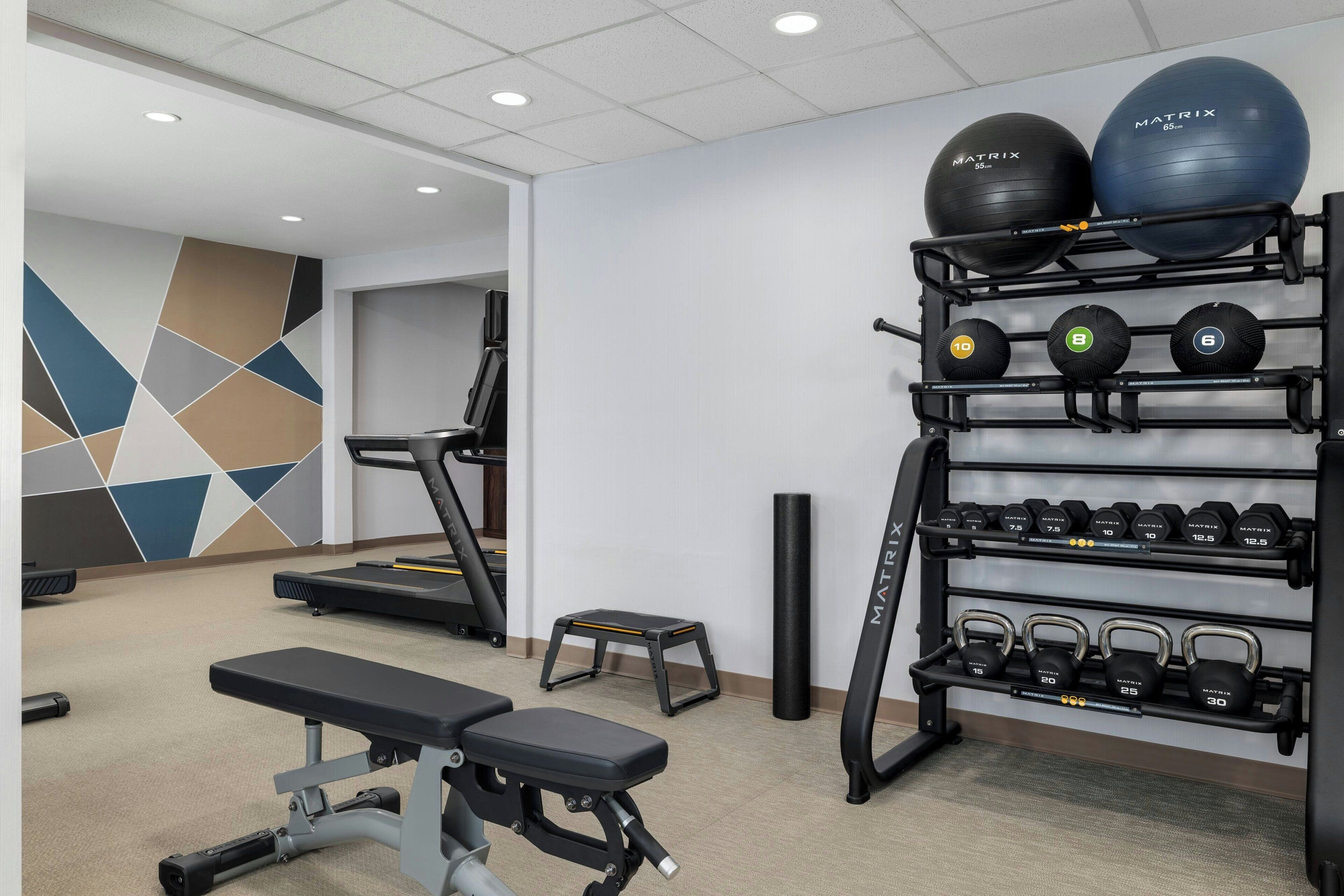 Een sportschool met loopbanden, een bank en een rek met dumbbells en medicijnballen.