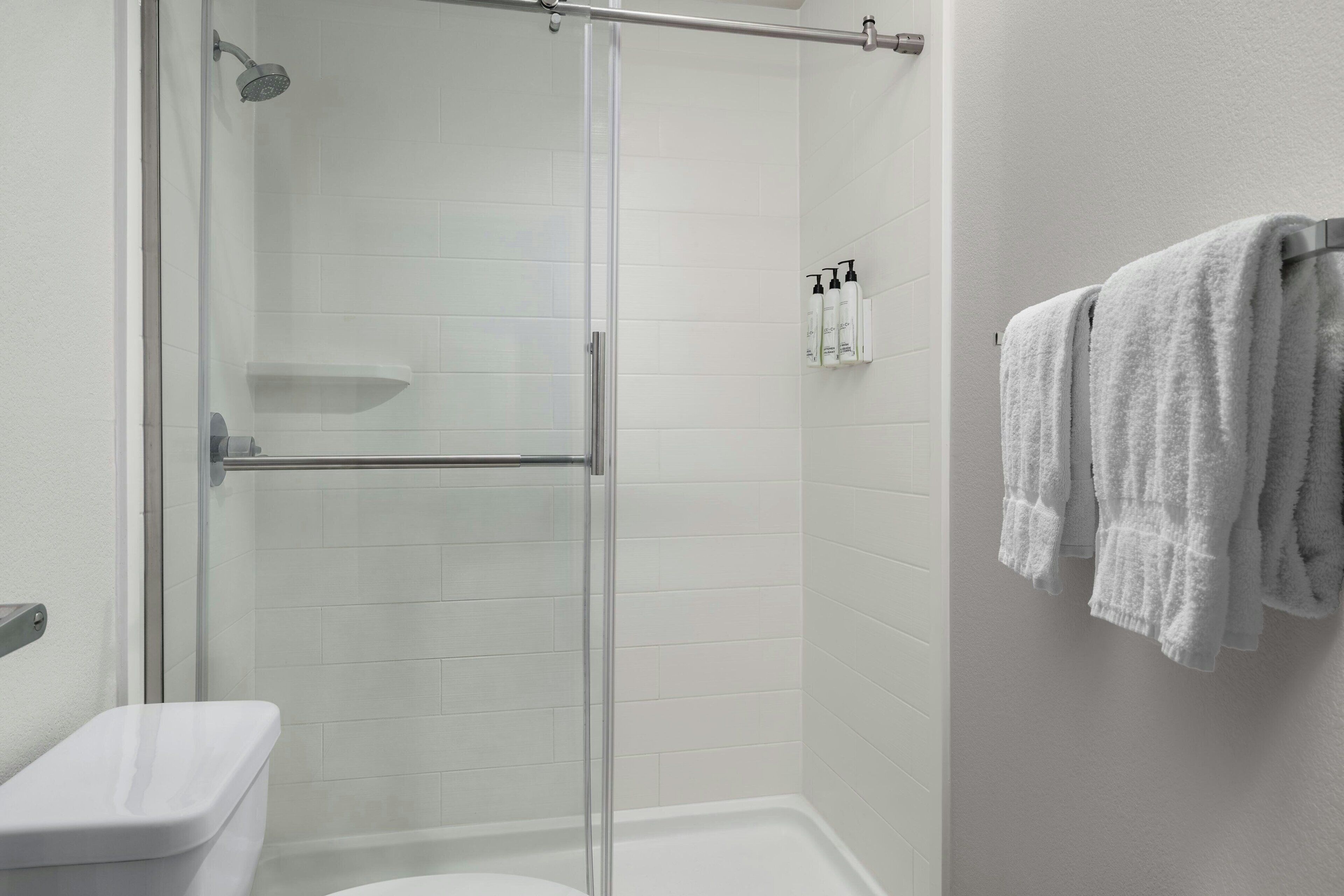 Un baño moderno con ducha de vidrio, azulejos blancos y un perchero con toallas.