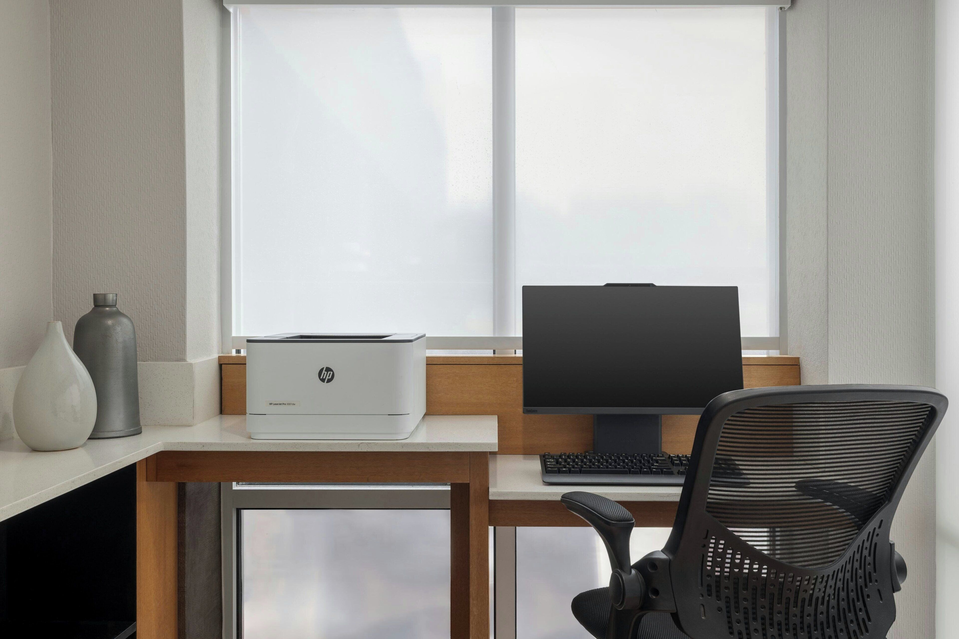A modern office desk with a printer, monitor, keyboard, and office chair.
