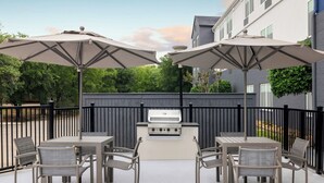 An outdoor patio with a grill, tables, chairs, and umbrellas. - SpringHill Suites Dallas Arlington North (Arlington)