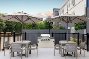 En udendørs terrasse med grill, borde, stole og parasoller.