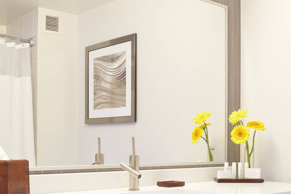 Une salle de bain moderne avec un meuble-lavabo blanc, un grand miroir et une œuvre d’art encadrée.
