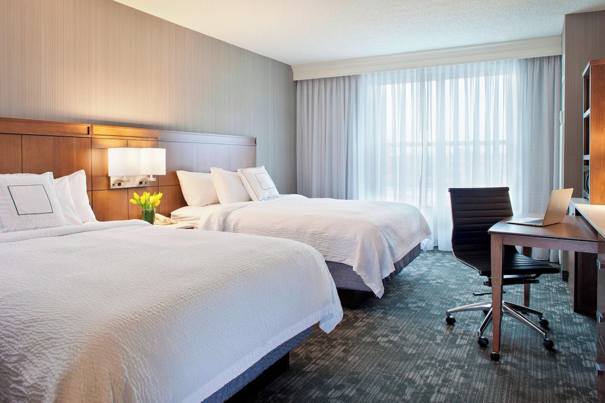 Une chambre d’hôtel avec deux lits, un bureau et une chaise.
