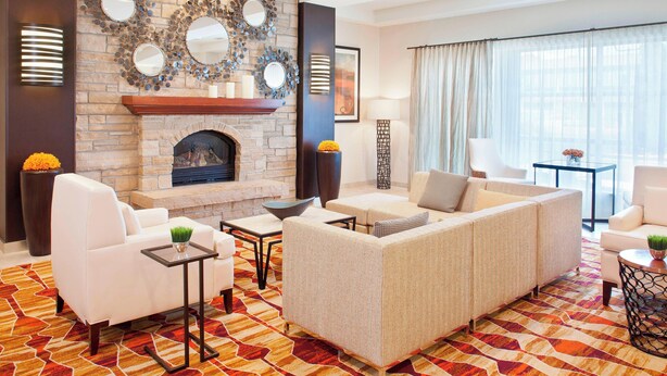 A modern living room with a stone fireplace, white sofas, and a patterned rug. - Courtyard by Marriott Pueblo Downtown (Pueblo)