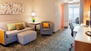 A hotel room with a sofa, armchair, small table with a lamp, and a desk with a laptop. - Courtyard by Marriott Pueblo Downtown (Pueblo)