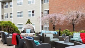 An outdoor seating area with wicker furniture, a barbecue grill, and a view of a building with multiple windows and a brick wall. - Residence Inn by Marriott Portsmouth (Portsmouth)