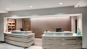 A reception area with two reception desks, a patterned wall, and a small plant on each desk. - Residence Inn by Marriott Portsmouth (Portsmouth)