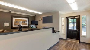 A reception desk with a 'WELCOME' sign, a clock, and a door leading outside.