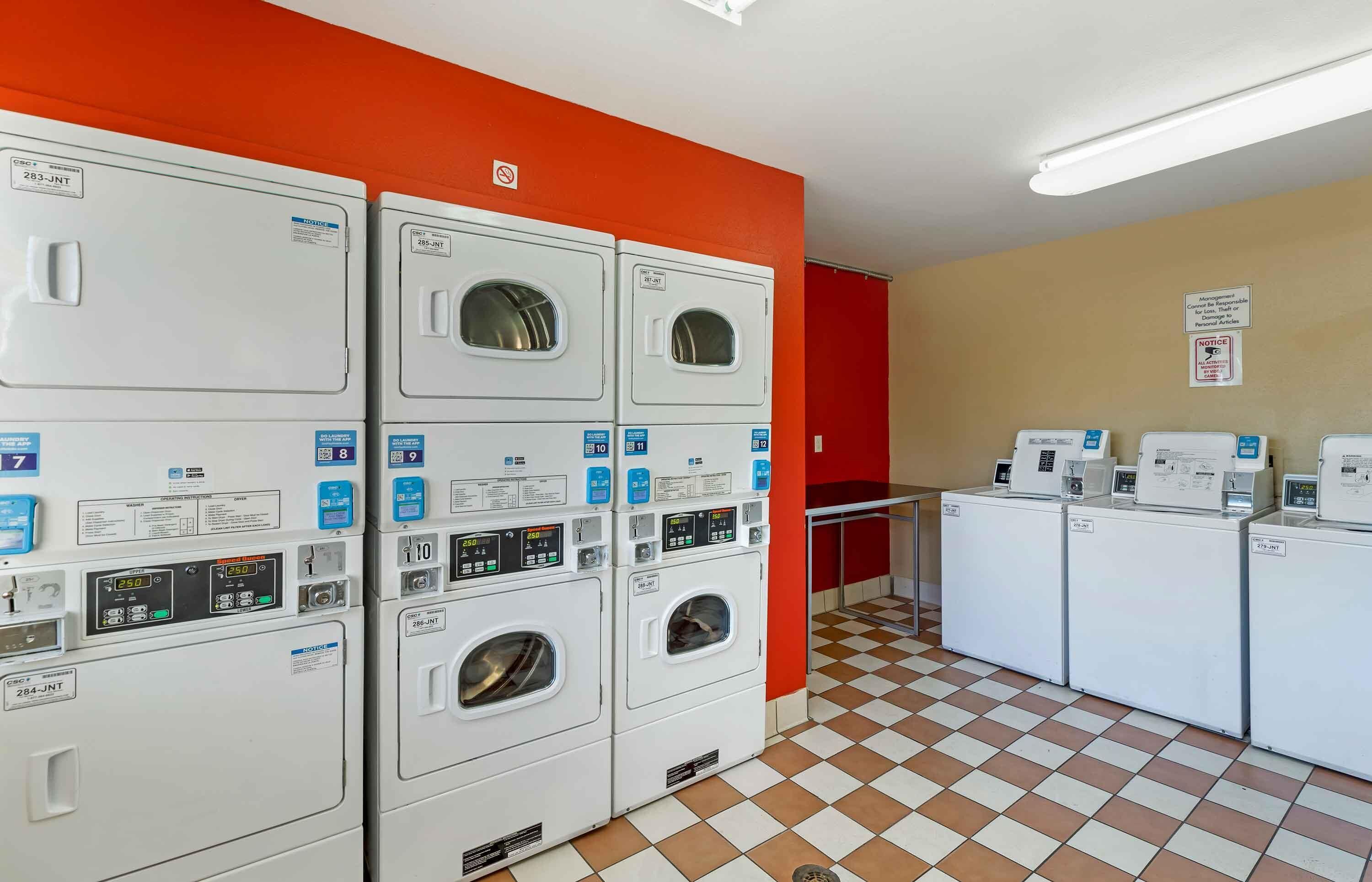 Een wasserette met meerdere wasmachines en drogers, een zwart-witte vloer en een rode muur.