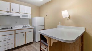 A compact kitchen with white cabinets, a microwave, a refrigerator, a sink, and a wooden chair.