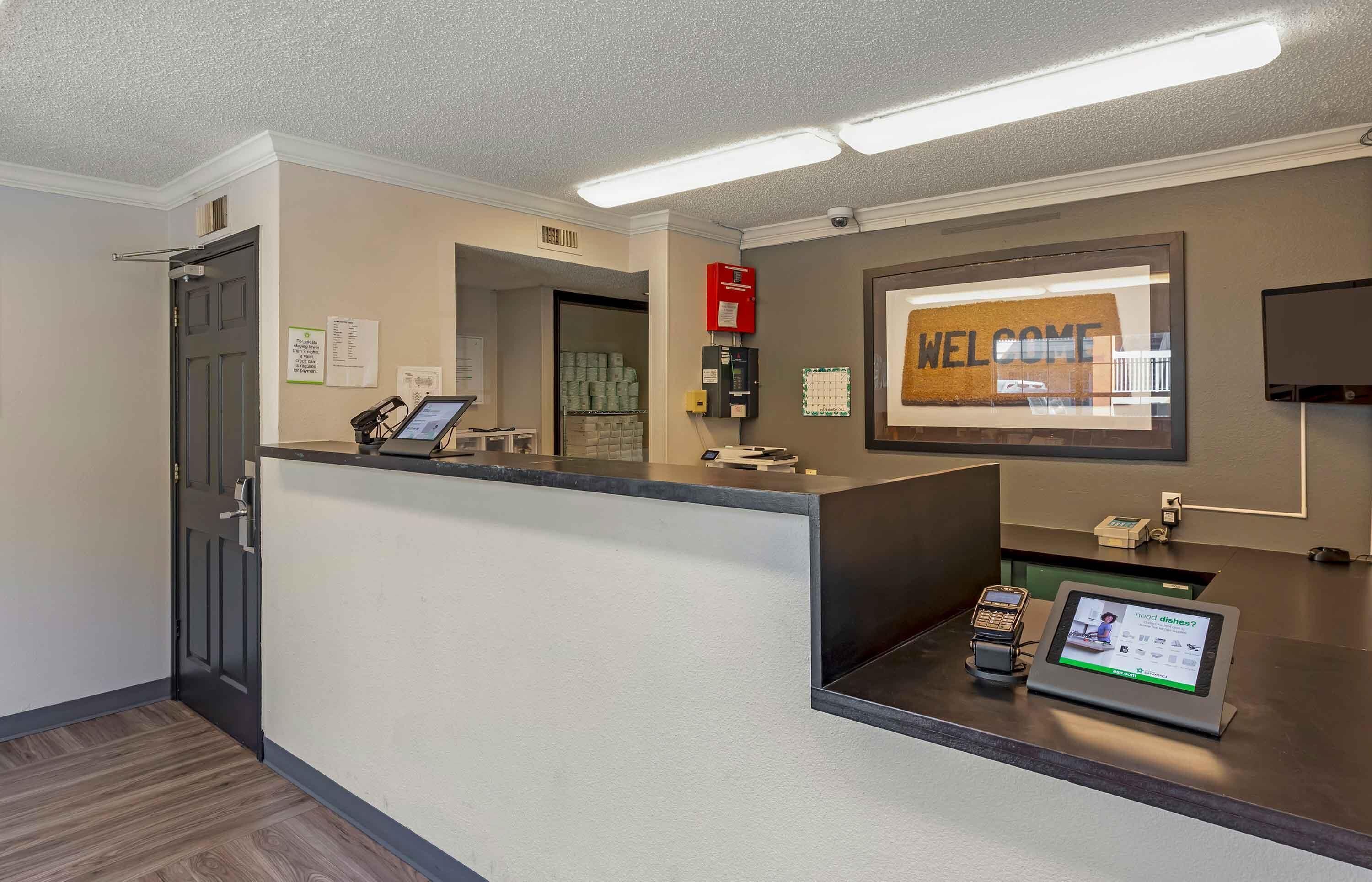 A reception desk with a 'WELCOME' sign, a phone, a digital kiosk, and a fire alarm.
