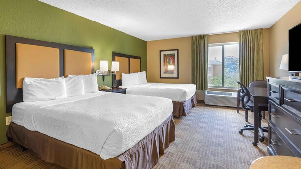 A hotel room with two beds, a desk, a chair, and a large window.