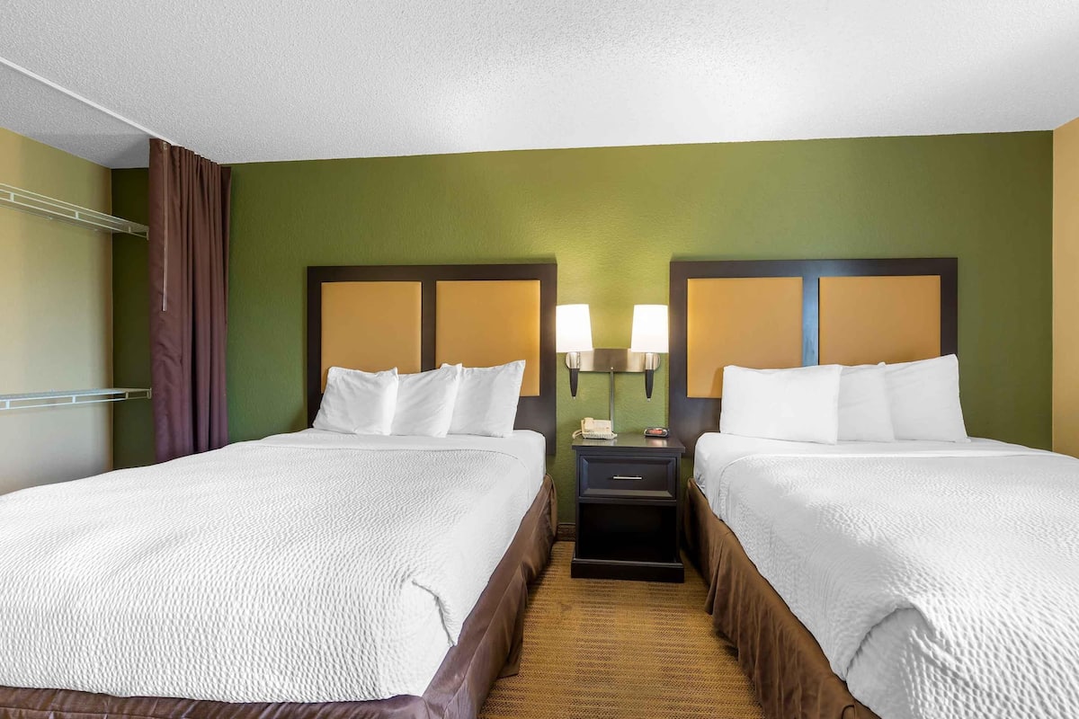 A hotel room with two beds, a nightstand with lamps, and a green wall.