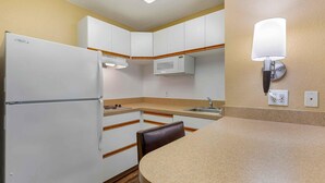 A compact kitchen with white cabinets, a built-in microwave, a refrigerator, and a wall-mounted light fixture.