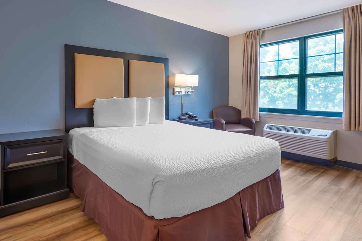 Une chambre d’hôtel avec un grand lit, un bureau avec une lampe, une chaise et une fenêtre avec des rideaux.