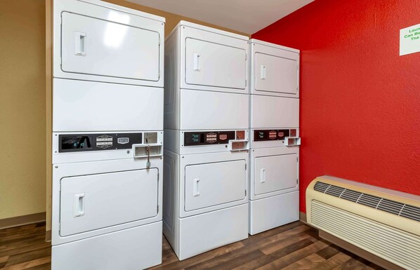 Un lavadero con lavadoras y secadoras apiladas, una pared roja y un radiador blanco.