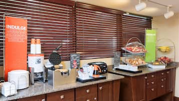 A breakfast buffet with waffle makers, coffee machines, and a variety of food items.