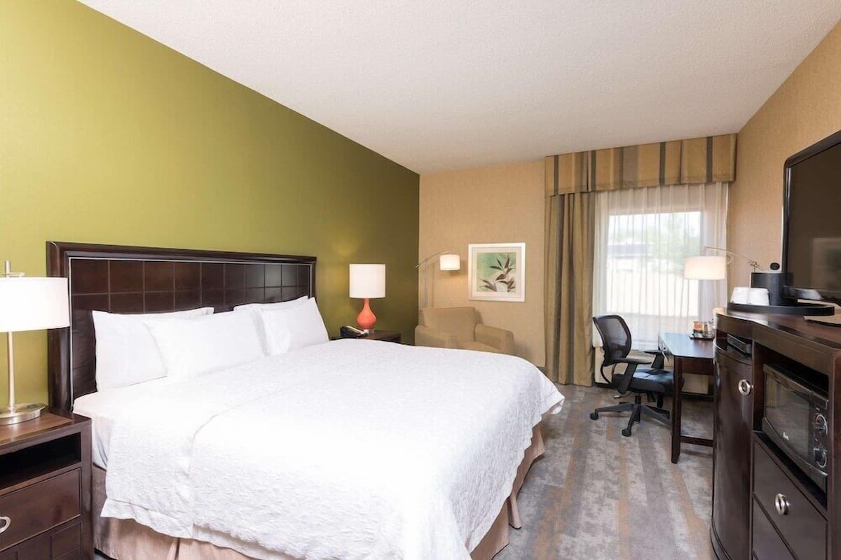 A hotel room with a large bed, a desk with a chair, a television, and a window with curtains.