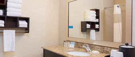 Et hotelbadeværelse med en vask på en granitbordplade, et spejl, et håndklædestativ med foldede håndklæder og et toilet.