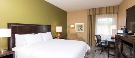 A hotel room with a large bed, a desk, a chair, a television, and a lamp.