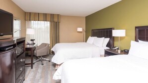 Een hotelkamer met twee bedden, een bureau met lamp, een stoel, een televisie en een dressoir.