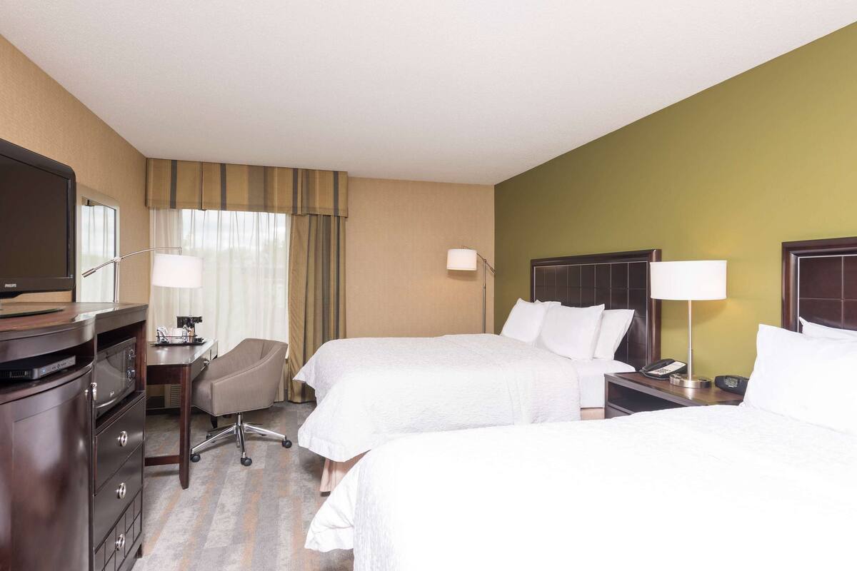 A hotel room with two beds, a desk with a lamp, a chair, a TV, and a dresser.
