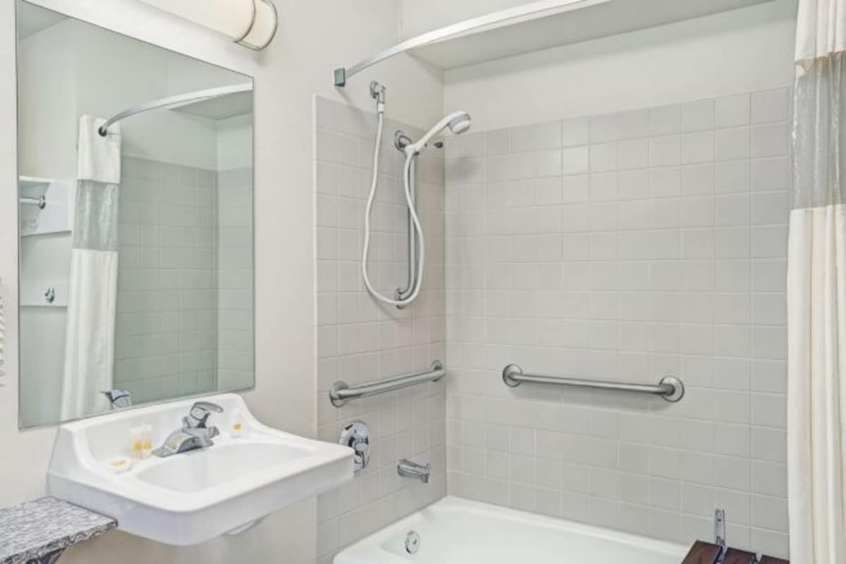 A bathroom with a sink, mirror, shower, and grab bars.