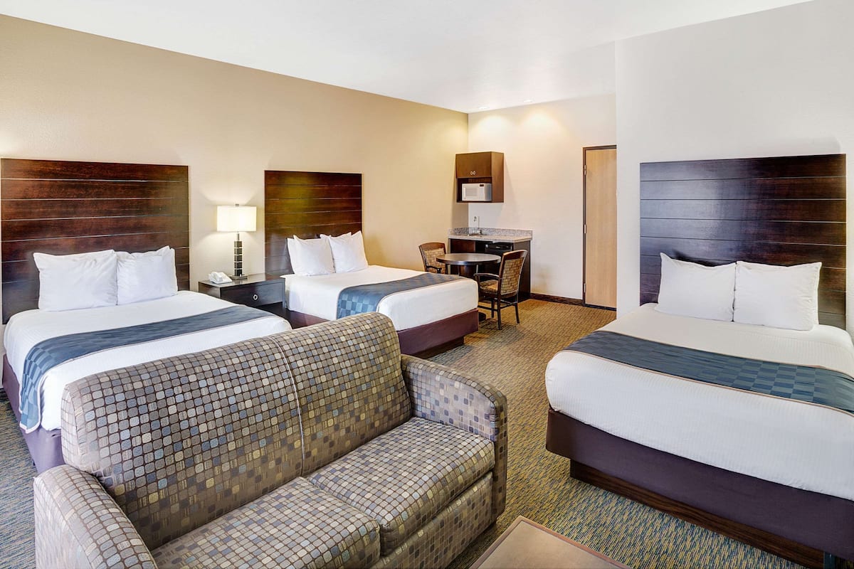 A hotel room with two beds, a sofa, a desk, and a microwave.
