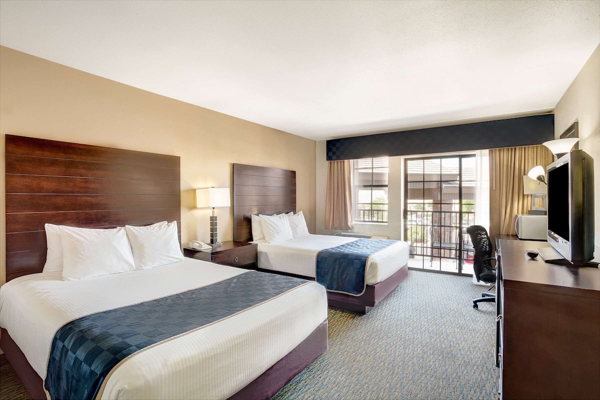 A hotel room with two beds, a desk, a TV, and a window with curtains.