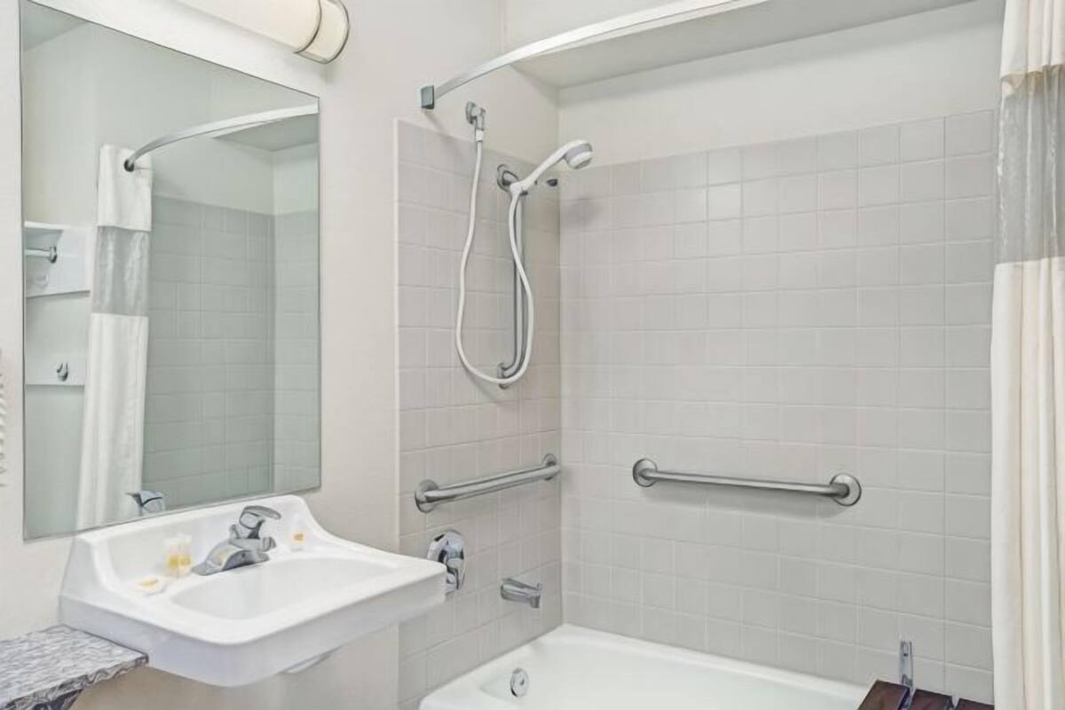 A bathroom with a sink, mirror, shower, and grab bars.