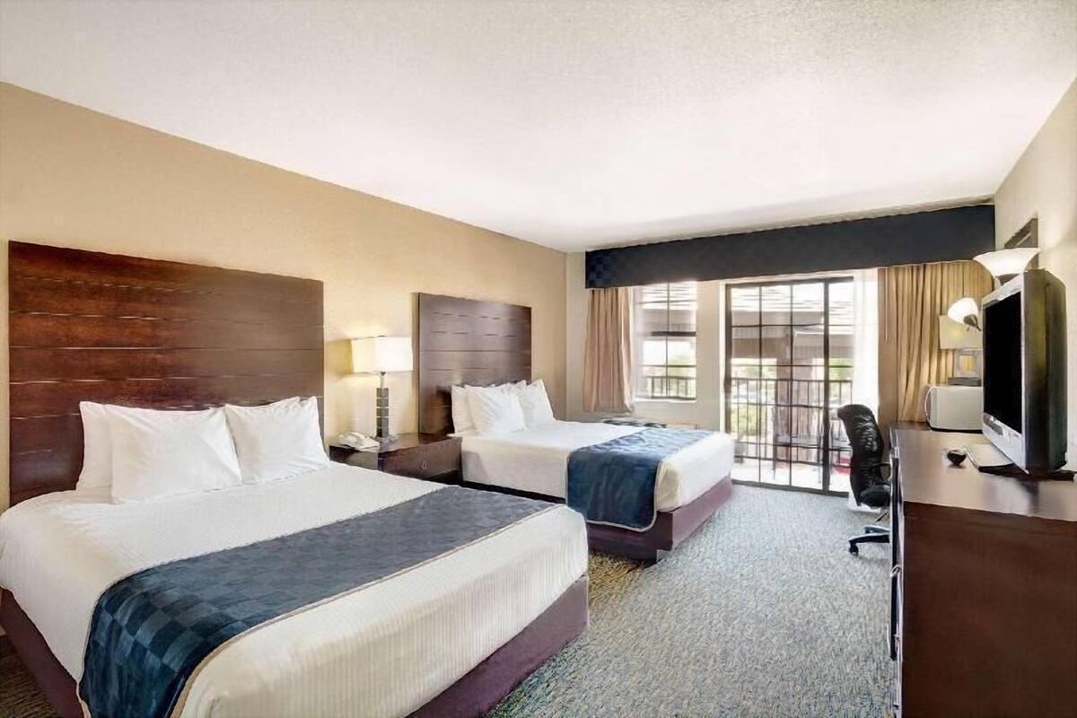 A hotel room with two beds, a desk, a TV, and a large window.