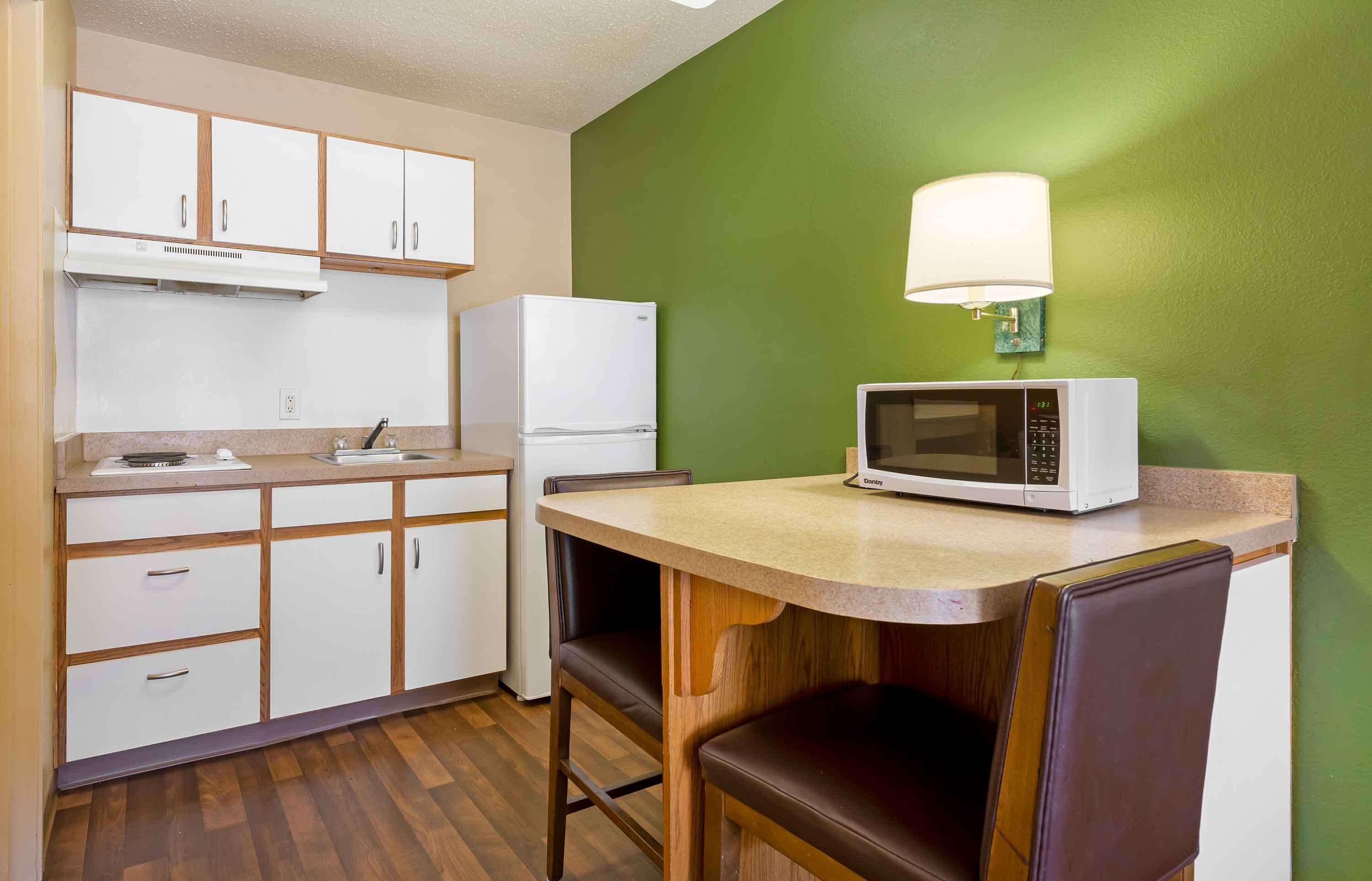 A compact kitchen with white cabinets, a microwave, a refrigerator, and a table with two chairs.