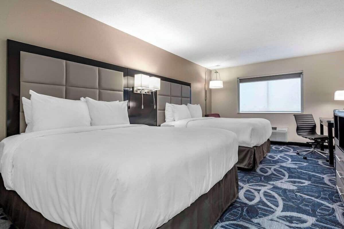 A hotel room with two beds, a desk, a chair, and a large window.