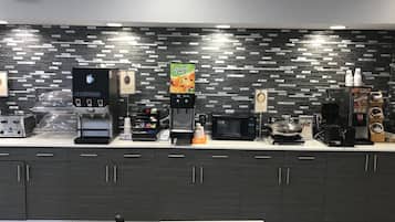 A self-service coffee station with various coffee machines, a microwave, and a food display.