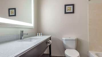 A modern bathroom with a white sink, mirror, and toilet. There are framed pictures on the wall and a roll of toilet paper on the counter.