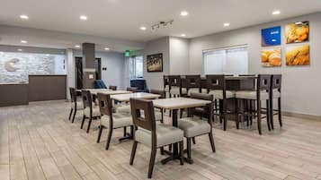 Un área de comedor moderna con varias mesas y sillas, una recepción y una pared con cuadros.
