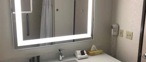 A bathroom with a large mirror, a sink, a towel rack, a hairdryer, and a tissue box.