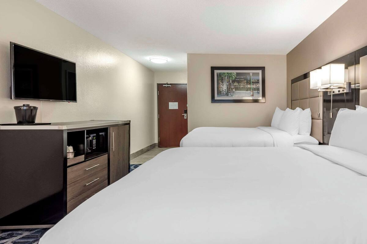 A hotel room with two beds, a TV, a desk, and a framed picture on the wall.